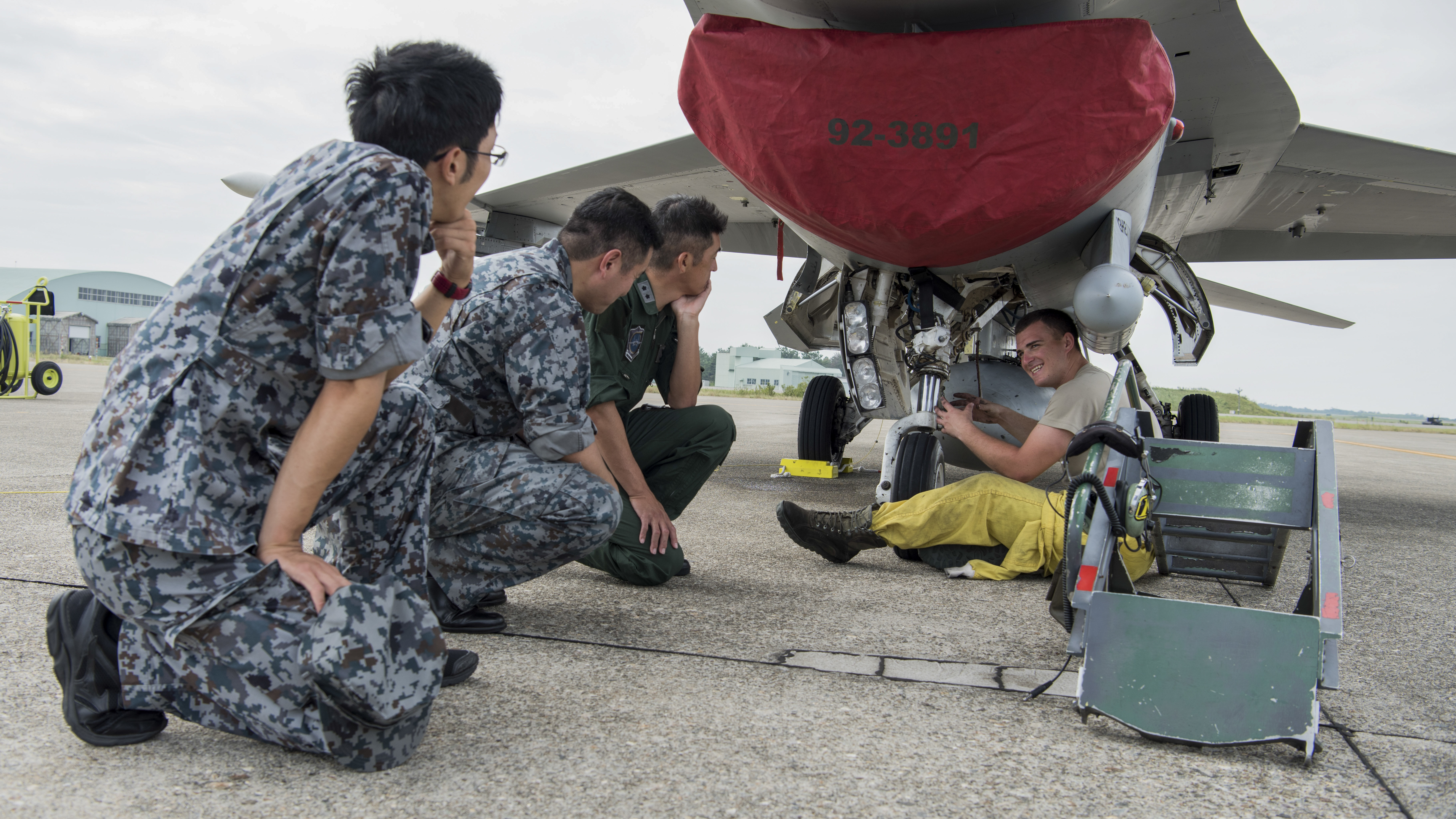 a 13th Aircraft Maintenance Unit dedicated crew chief, shows Major General Masahito Monma, the Japan Air Self-Defense Force 6th Air Wing commander, a nose wheel steering system on an F-16 Fighting Falcon during an aviation training relocation at Komatsu Air Base, Japan